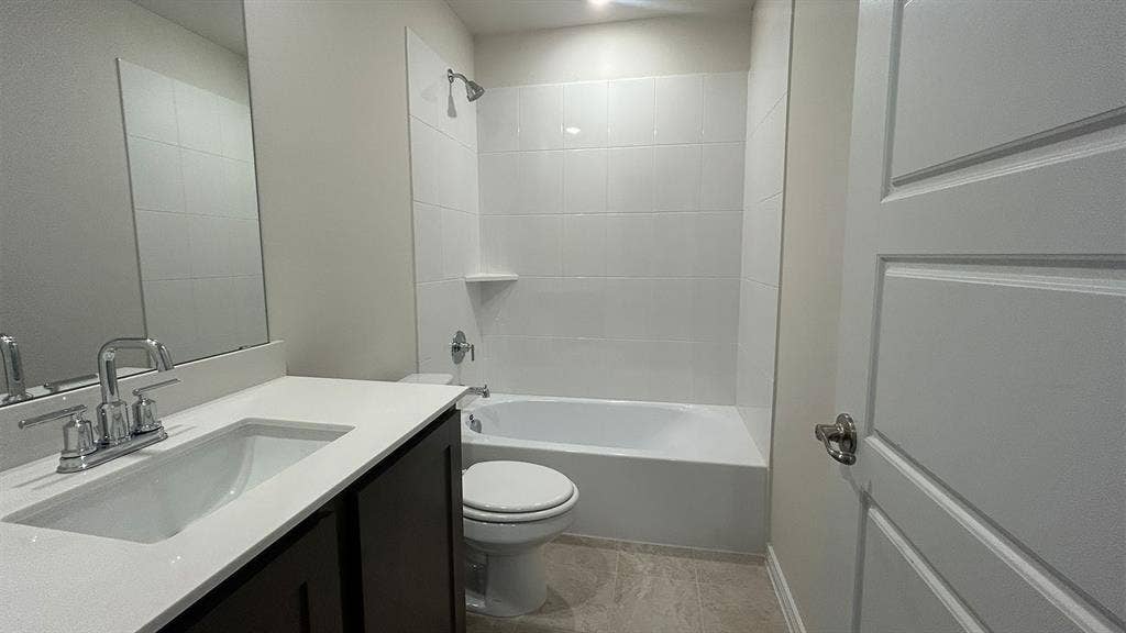 410 Campfield Drive, Caddo Mills, TX 75135 Dark cabinetry vanity with a solid-surface countertop and integrated sink, complemented by a white-tiled shower-tub combination and a large wall-mounted mirror