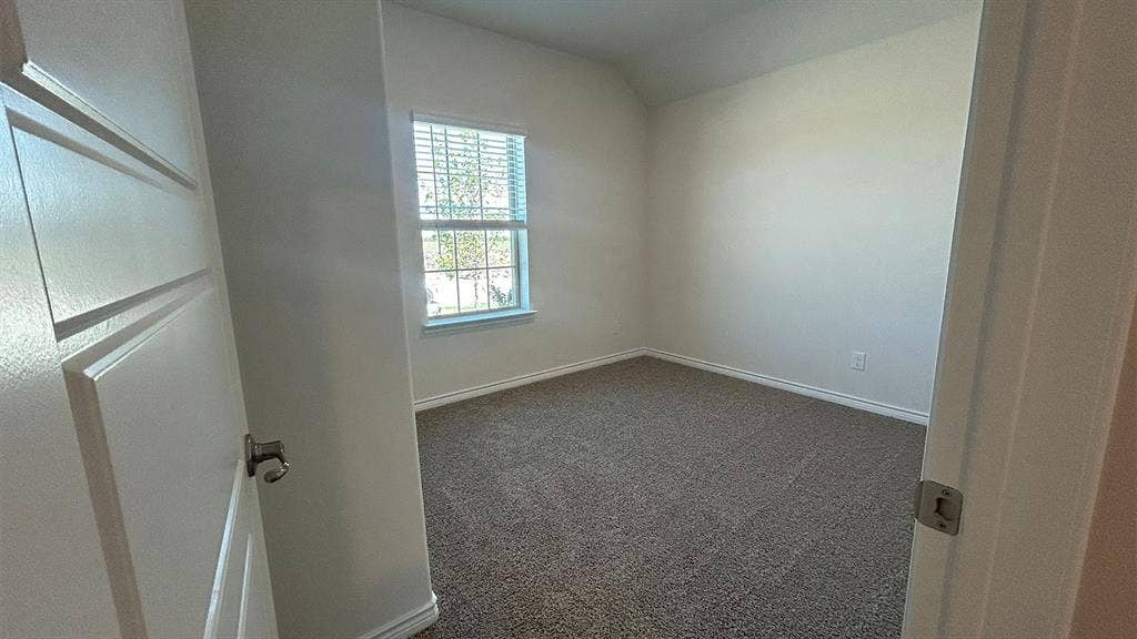 410 Campfield Drive, Caddo Mills, TX 75135 Neutral-toned room featuring neutral carpeting, a single-panel window with muntins, a vaulted ceiling, and a multi-panel door with metallic hardware