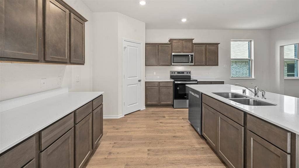 5727 Sunshine Lane, Crandall, TX 75114 Kitchen featuring an expansive island with a double basin sink, stainless steel appliances, wood-finish flooring, white countertops, and shaker-style cabinetry