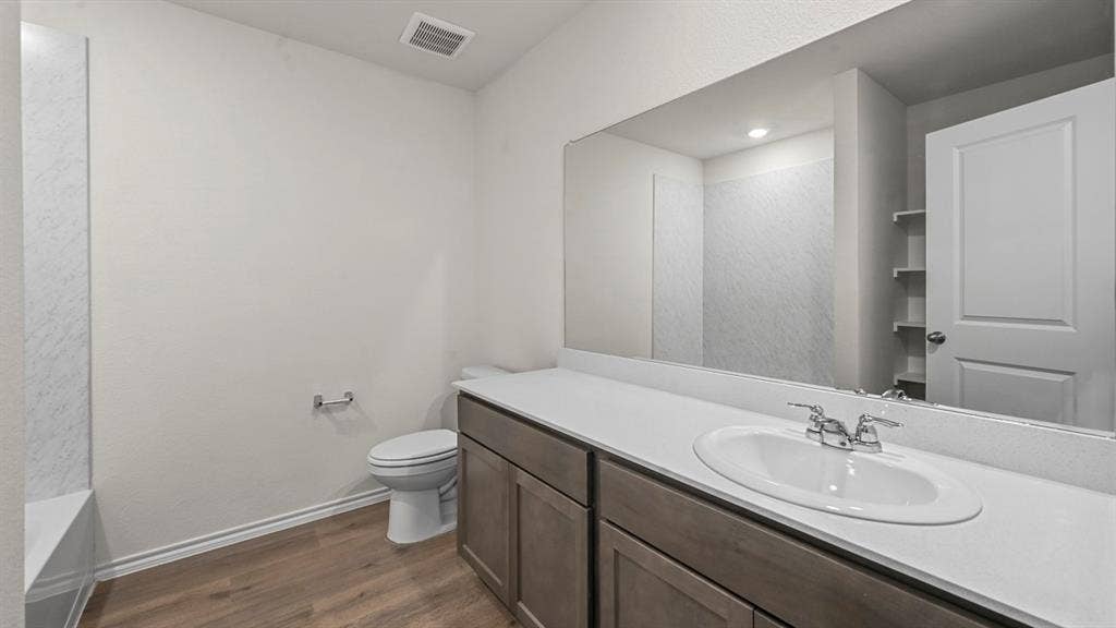 5727 Sunshine Lane, Crandall, TX 75114 Bathroom featuring a wood-finish flooring, a vanity with a white countertop and integrated sink, a large wall-mounted mirror, and a built-in shower/tub combination with a tiled surround