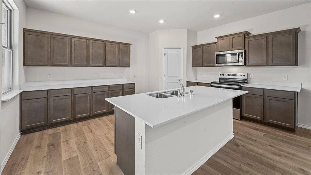 5727 Sunshine Lane, Crandall, TX 75114 Kitchen featuring an island with dual sinks, extensive dark wood-finish cabinetry, light-toned countertops, stainless steel appliances, and recessed lighting
