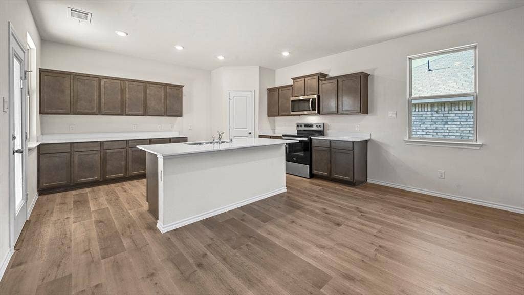 5727 Sunshine Lane, Crandall, TX 75114 Kitchen featuring wood-finish flooring, white countertops, dark wood-finish cabinetry, stainless steel appliances, and a central island with sink