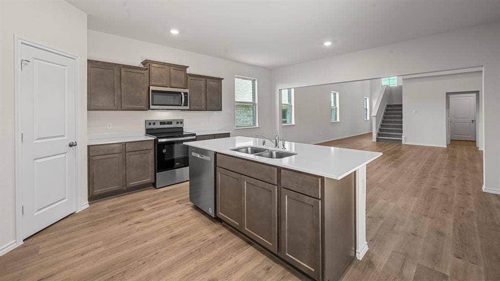 5727 Sunshine Lane, Crandall, TX 75114 Spacious kitchen featuring an island with a double basin sink, stainless steel appliances, dark wood-finish cabinetry, and light-tone wood-finish flooring