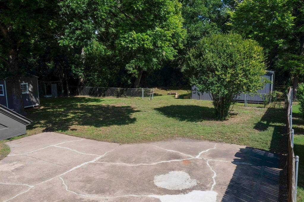 550 Glen Oaks Boulevard, Dallas, TX 75232 Backyard featuring a concrete patio, chain-link fencing, mature trees, and two detached storage structures