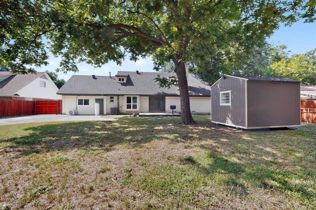 550 Glen Oaks Boulevard, Dallas, TX 75232 Expansive backyard featuring a mature shade tree, detached storage structure, concrete driveway, and wooden perimeter fencing