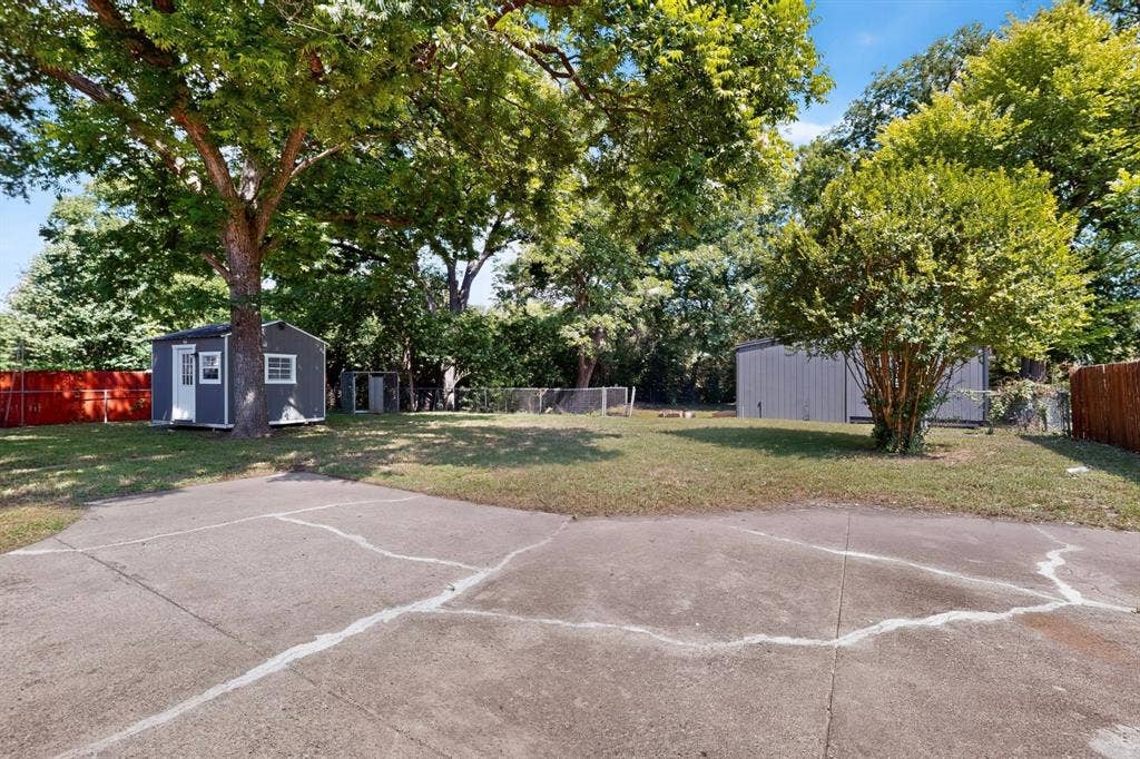 550 Glen Oaks Boulevard, Dallas, TX 75232 Expansive backyard featuring mature trees, a concrete parking area, a detached storage structure, and perimeter fencing