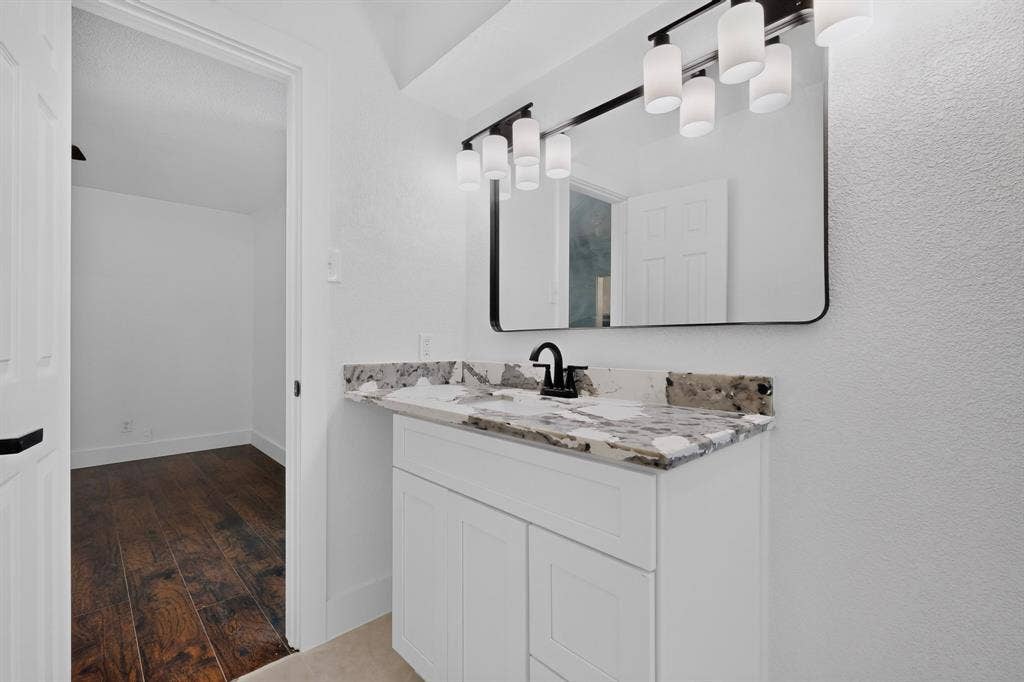 550 Glen Oaks Boulevard, Dallas, TX 75232 White vanity featuring stone-finish countertop with undermount sink, matte black faucet, wall-mounted rectangular mirror, and five-light vanity fixture