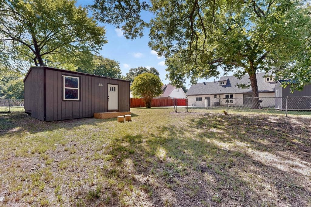550 Glen Oaks Boulevard, Dallas, TX 75232 Expansive backyard featuring a detached structure with siding, chain-link perimeter fencing, mature trees, and a multi-section roofline