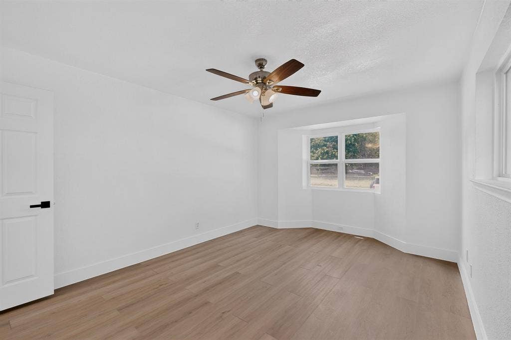 550 Glen Oaks Boulevard, Dallas, TX 75232 Room featuring wood-finish flooring, a bay window, a ceiling fan with integrated lighting, and a door with matte black hardware