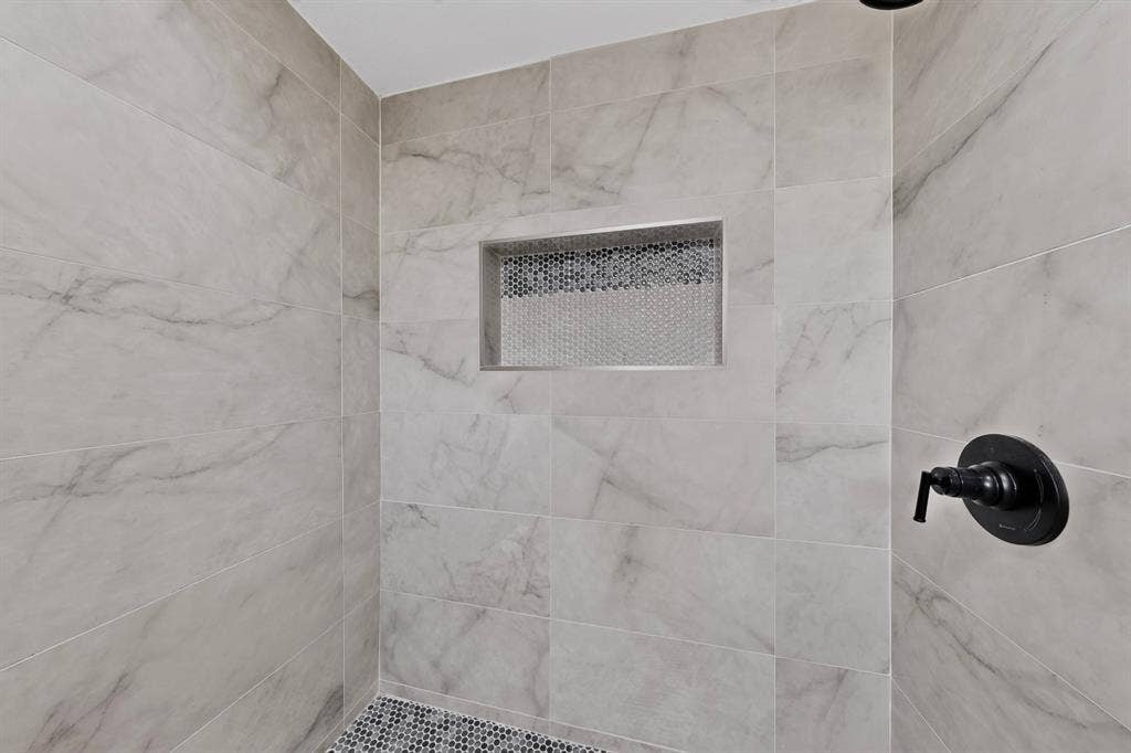 550 Glen Oaks Boulevard, Dallas, TX 75232 Shower enclosure featuring large-format stone-patterned wall tile, a recessed tile niche with hexagonal accent mosaic, a circular black shower control valve, and a hexagonal tile floor