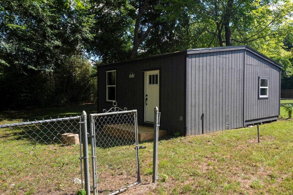 550 Glen Oaks Boulevard, Dallas, TX 75232 Detached structure featuring dark-toned vertical siding, a single-entry door with glass panels, multiple windows, and a surrounding chain-link fence