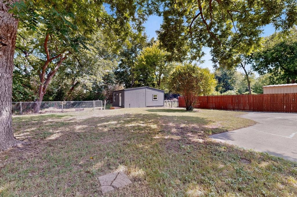 550 Glen Oaks Boulevard, Dallas, TX 75232 Expansive backyard featuring a concrete driveway, detached storage structure, mature trees, and combination metal and wood-style fencing