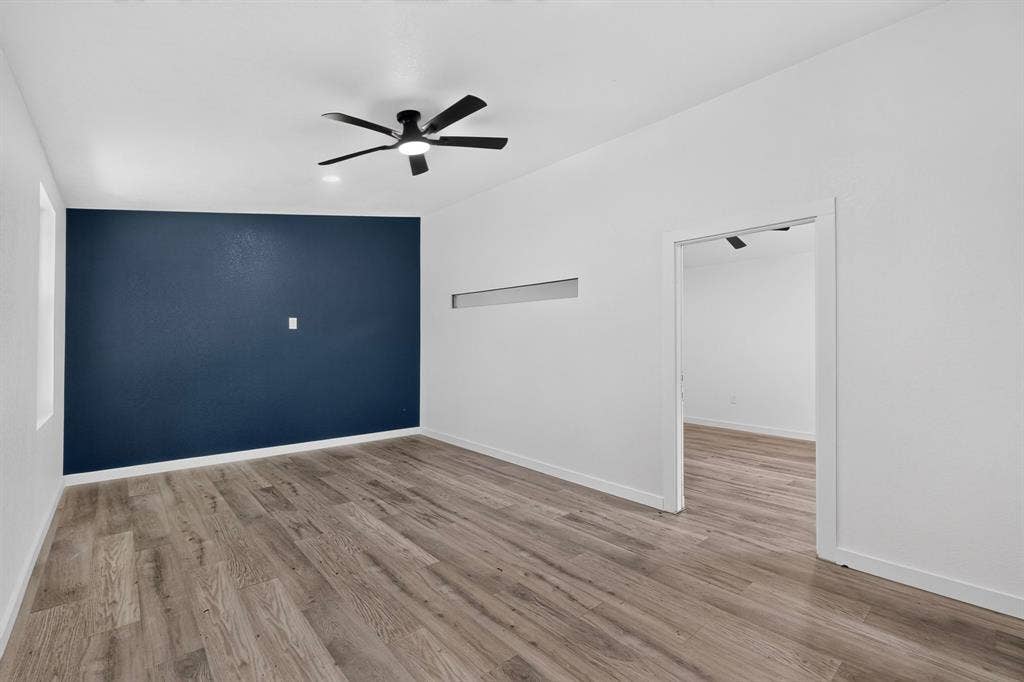 550 Glen Oaks Boulevard, Dallas, TX 75232 Interior space featuring wood-finish flooring, a dark-toned accent wall, a central ceiling fan with integrated lighting, and a horizontal transom window