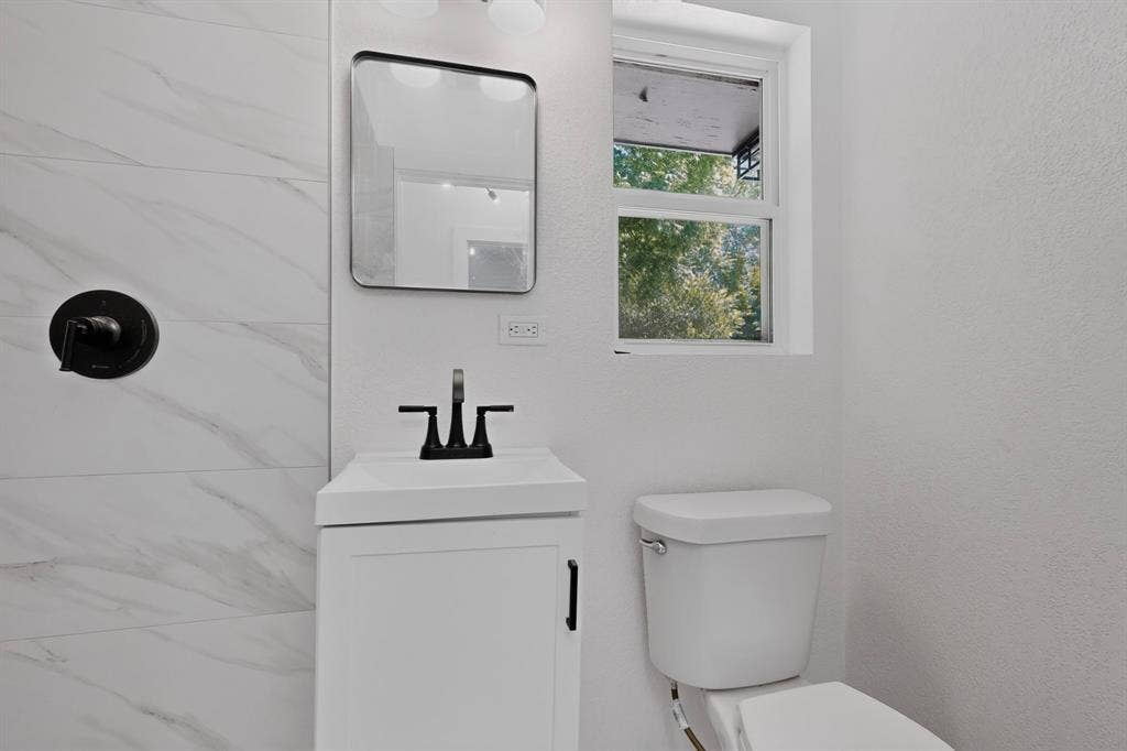 550 Glen Oaks Boulevard, Dallas, TX 75232 Bathroom featuring a white vanity cabinet, rectangular sink with matte black faucet, wall-mounted mirror, matte black shower handle, and tile surround with marbled finish