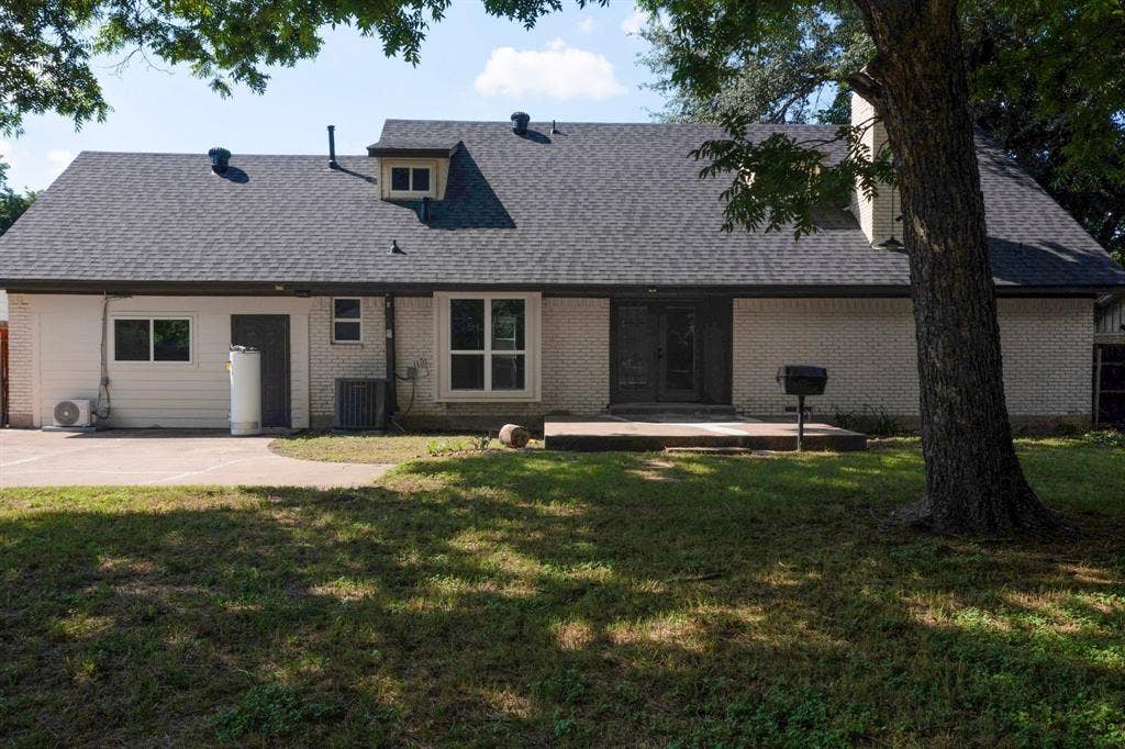 550 Glen Oaks Boulevard, Dallas, TX 75232 Rear exterior featuring white painted brick facade, asphalt shingle roofing, concrete patio, and mature trees