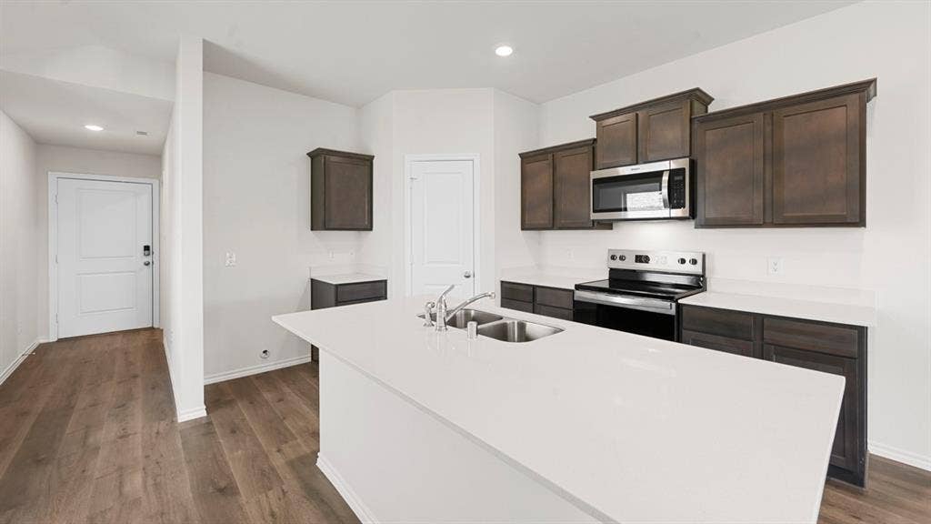 5731 Sunshine Lane, Crandall, TX 75114 Kitchen featuring wood-finish flooring, white countertops, dark wood cabinetry, stainless steel appliances, and a kitchen island with an undermount sink