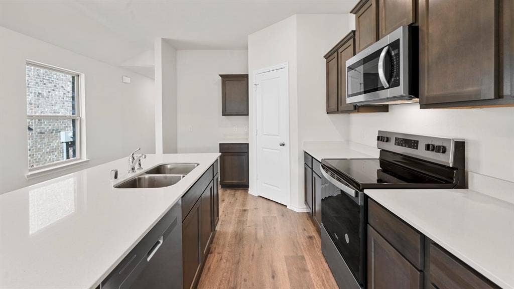 5731 Sunshine Lane, Crandall, TX 75114 Spacious kitchen featuring dark wood-finish cabinetry, light countertops, wood-finish flooring, a stainless steel double basin sink, and stainless steel appliances
