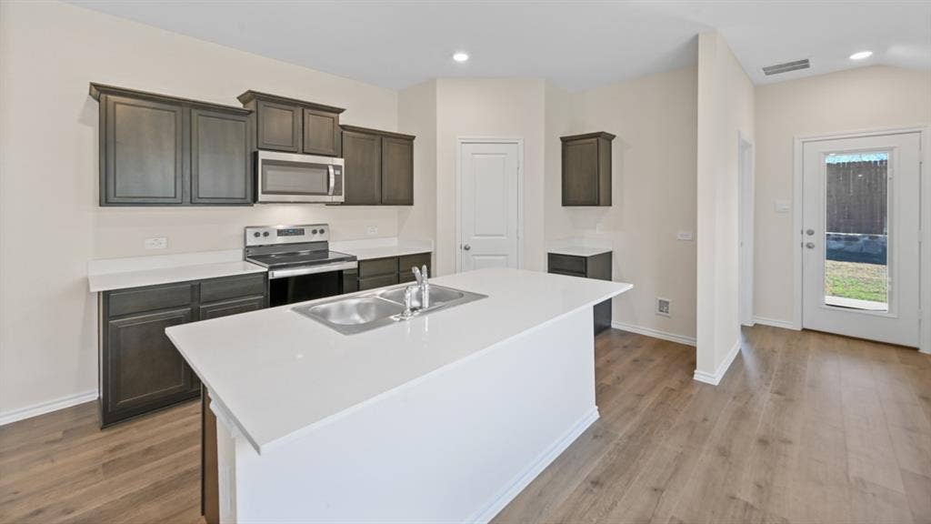 5739 Sunshine Lane, Crandall, TX 75114 Kitchen featuring a central island with a double basin sink, dark wood cabinetry, stainless steel appliances, light countertops, and wood-finish flooring