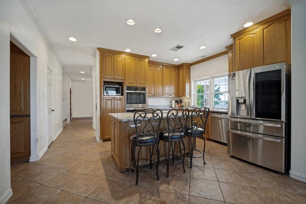 1957 E Fm 550, Rockwall, TX 75032 Kitchen featuring wood cabinetry, stone-surface countertops, a center island with bar seating, stainless steel appliances, and tile flooring