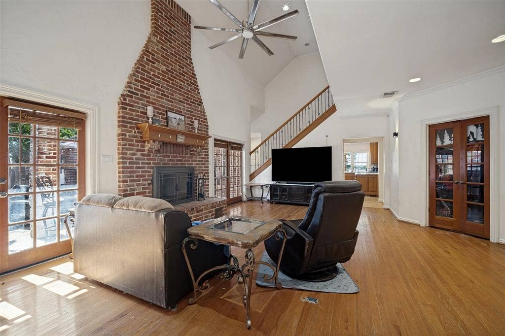 1957 E Fm 550, Rockwall, TX 75032 Vaulted ceiling featuring a multi-blade ceiling fan, exposed brick fireplace with a wood mantel, wood-finish flooring, staircase with wood railing, and French doors