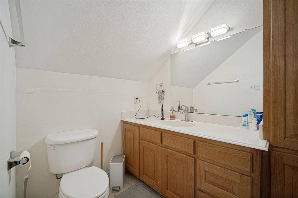 1957 E Fm 550, Rockwall, TX 75032 Bathroom featuring a wood-finish vanity with a solid-surface integrated sink, large wall-mounted mirror, three-light fixture, and architectural sloped ceiling