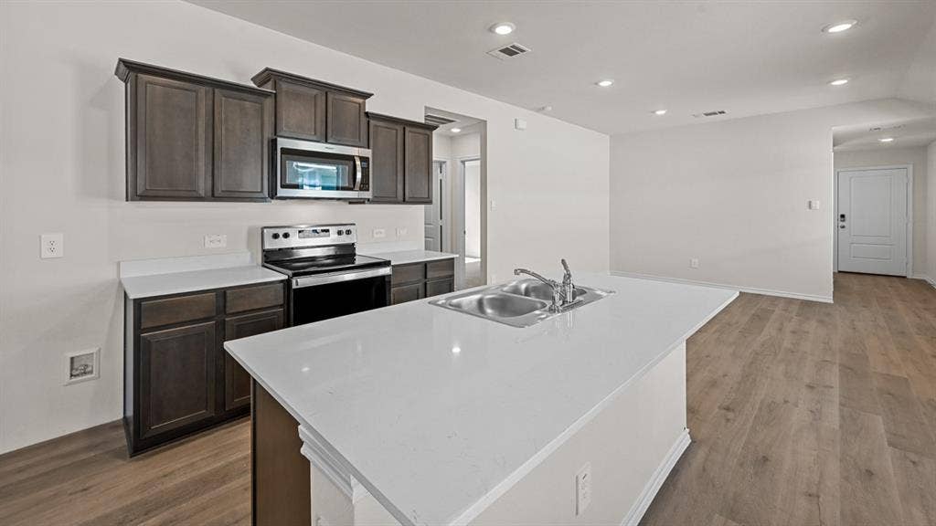 5743 Sunshine Lane, Crandall, TX 75114 Kitchen featuring wood-finish cabinetry, stainless steel appliances, a center island with an integrated sink, and white countertops