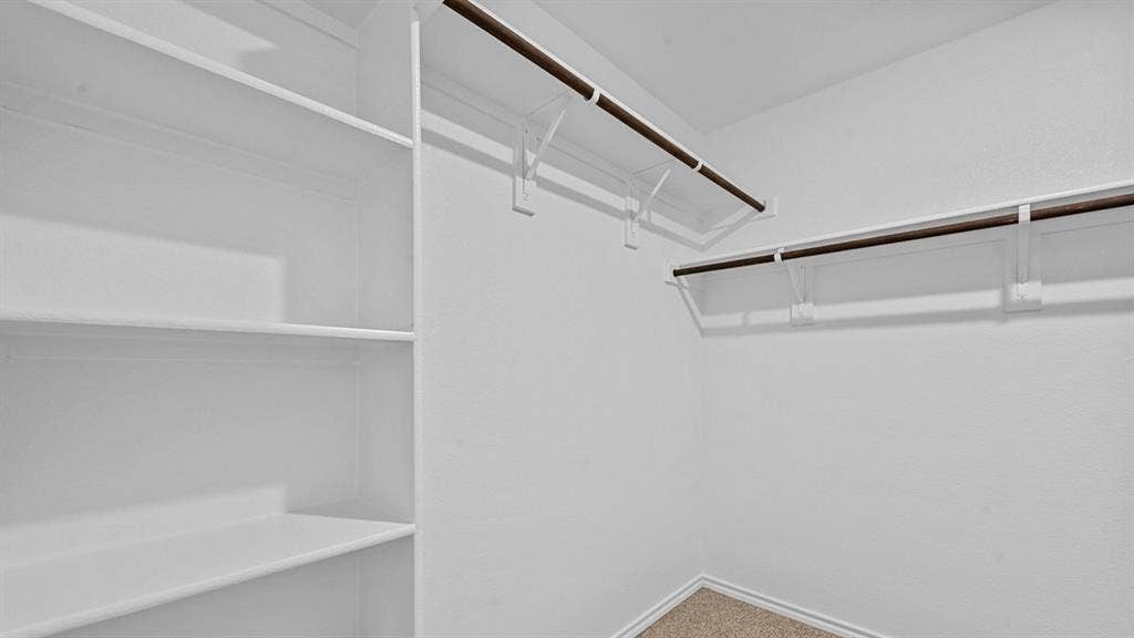 5743 Sunshine Lane, Crandall, TX 75114 Spacious walk-in closet featuring built-in shelving, dual hanging rods with metal brackets, and wood-finish flooring throughout