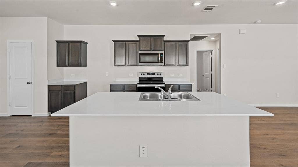 5743 Sunshine Lane, Crandall, TX 75114 Spacious kitchen with a central island featuring an integrated stainless steel sink, dark wood-finish cabinetry, light-toned countertops, and wood-finish flooring