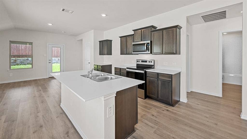 5743 Sunshine Lane, Crandall, TX 75114 Kitchen island with dual basin sink, white countertops, wood-finish flooring, dark wood cabinetry, and stainless steel appliances