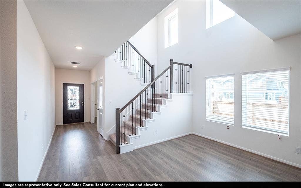 Double-height ceiling, staircase with dark wood-finish handrail and metal balusters, wood-finish flooring, and windows with integrated blinds