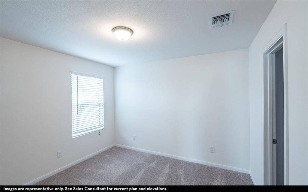 Neutral-toned interior space featuring wall-to-wall carpeting, a flush-mount overhead light fixture, and a window with horizontal blinds