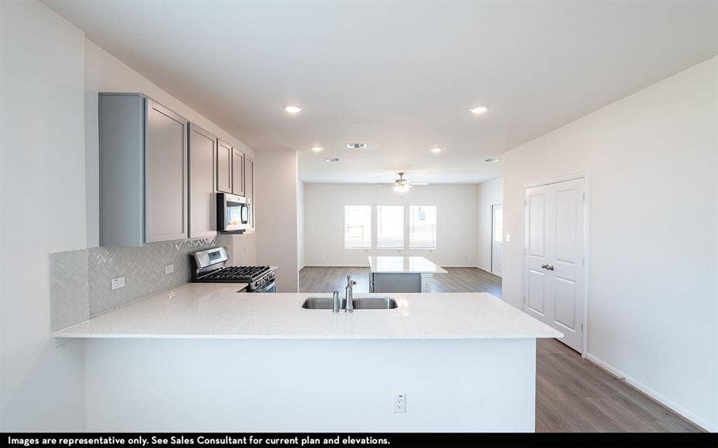 Kitchen featuring shaker-style cabinetry, quartz countertops, herringbone-patterned tile backsplash, stainless steel gas range, and a center island with double-basin undermount sink
