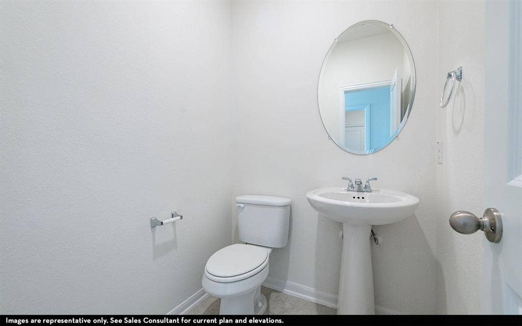 Powder room featuring a white pedestal sink, chrome hardware, oval wall-mounted mirror, and a standard-height toilet