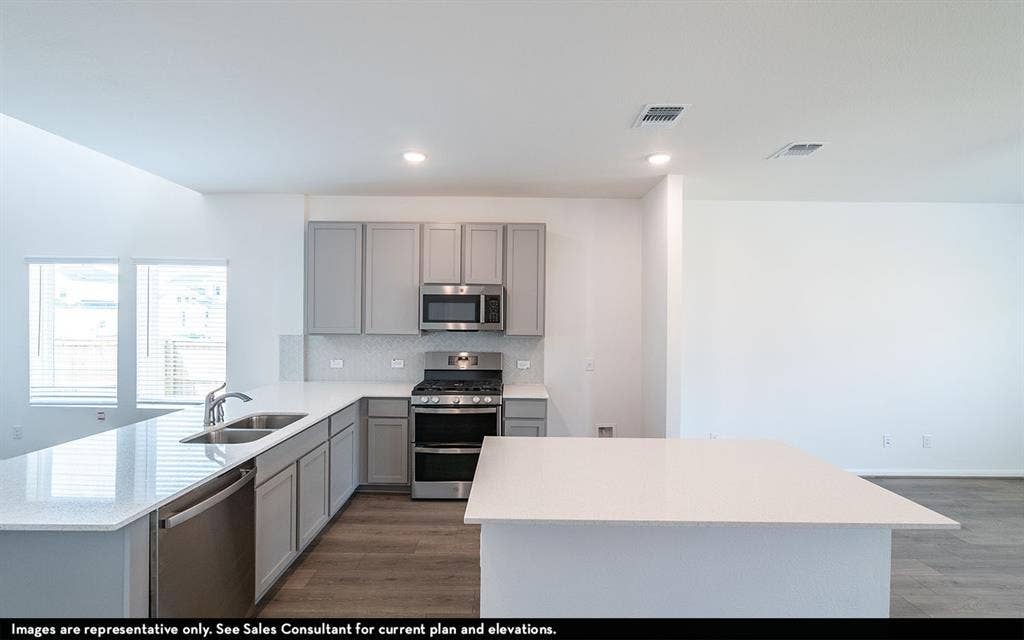 Kitchen featuring gray shaker-style cabinetry, quartz countertops, a central island, stainless steel appliance suite, and wood-finish flooring