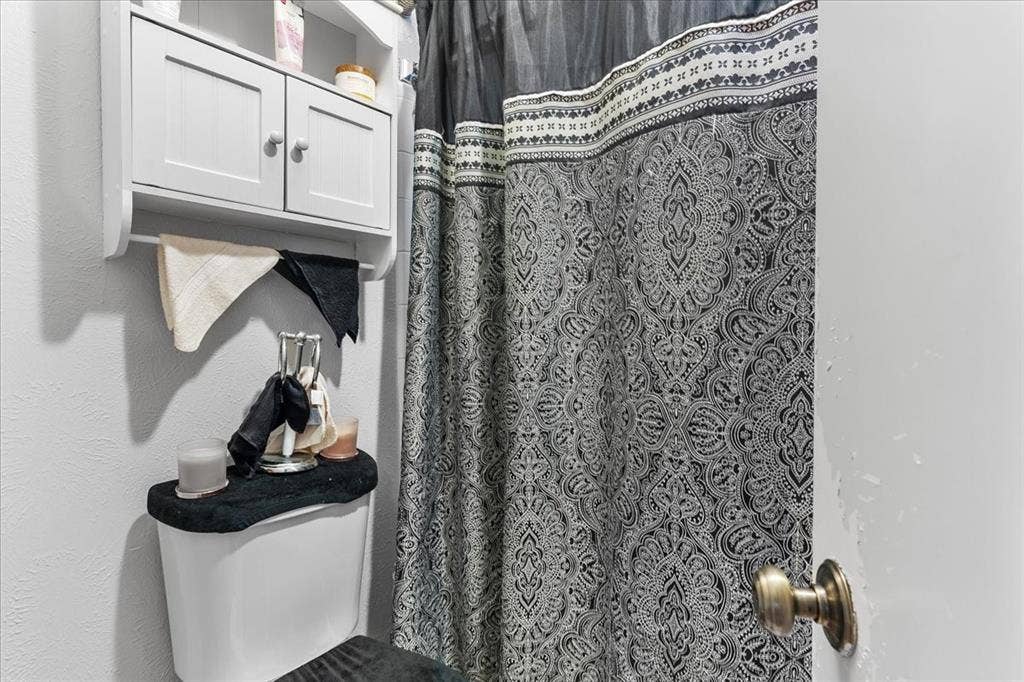 2702 Pebble Beach Drive, Lancaster, TX 75134 Wall-mounted wooden cabinet with dual doors and an open lower shelf, positioned above a standard toilet