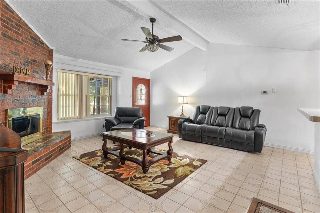 2702 Pebble Beach Drive, Lancaster, TX 75134 Vaulted ceilings with exposed beams, brick fireplace featuring a wood mantel and raised hearth, neutral tile flooring, and multi-paned glass entry door