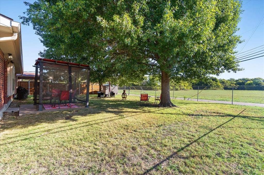 2702 Pebble Beach Drive, Lancaster, TX 75134 Spacious backyard featuring a large mature tree, a paved patio area, and perimeter chain-link fencing