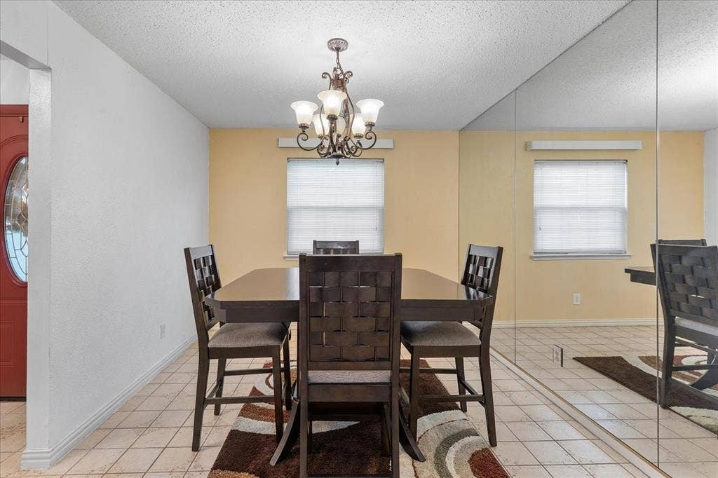 2702 Pebble Beach Drive, Lancaster, TX 75134 Dining area featuring large-scale wall mirrors, a multi-arm chandelier with glass shades, neutral ceramic tile flooring, and a window with blinds