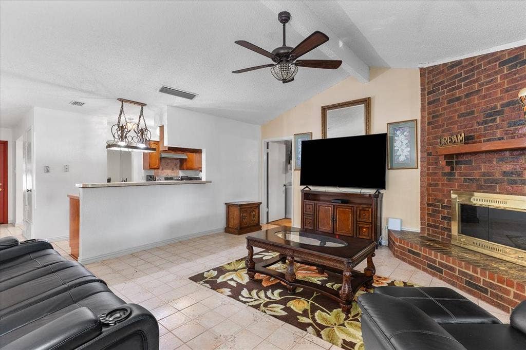 2702 Pebble Beach Drive, Lancaster, TX 75134 Living area featuring a floor-to-ceiling red brick fireplace with a wood mantel, vaulted ceilings with a center fan, tiled flooring, and a pass-through window with a breakfast bar