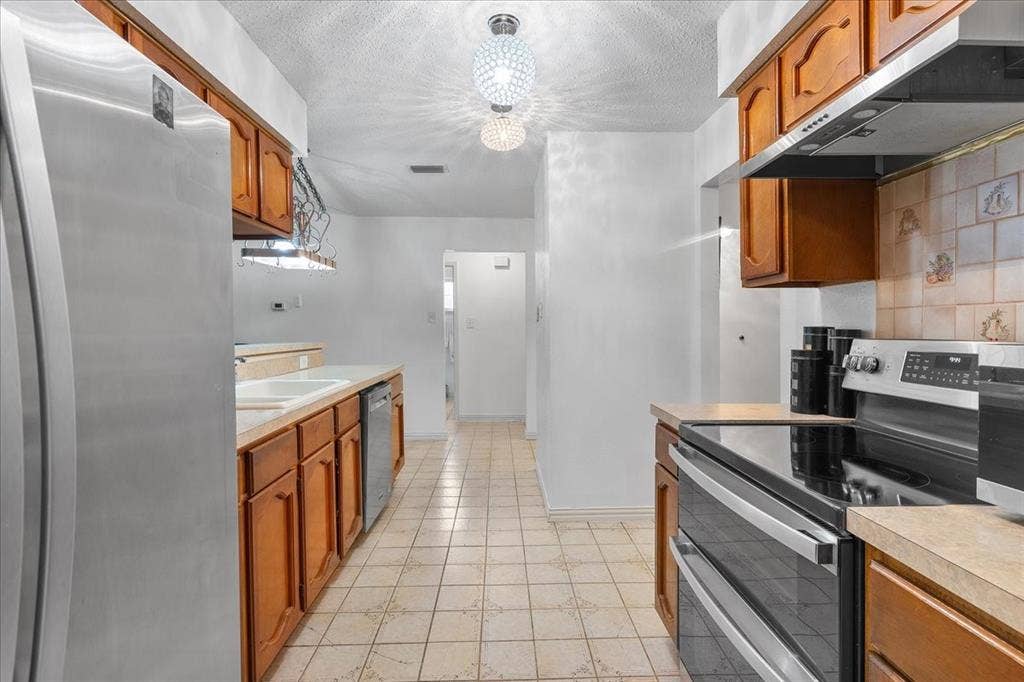 2702 Pebble Beach Drive, Lancaster, TX 75134 Kitchen featuring wooden cabinetry, stainless steel appliances, a tiled backsplash, and a spherical semi-flush mount light fixture