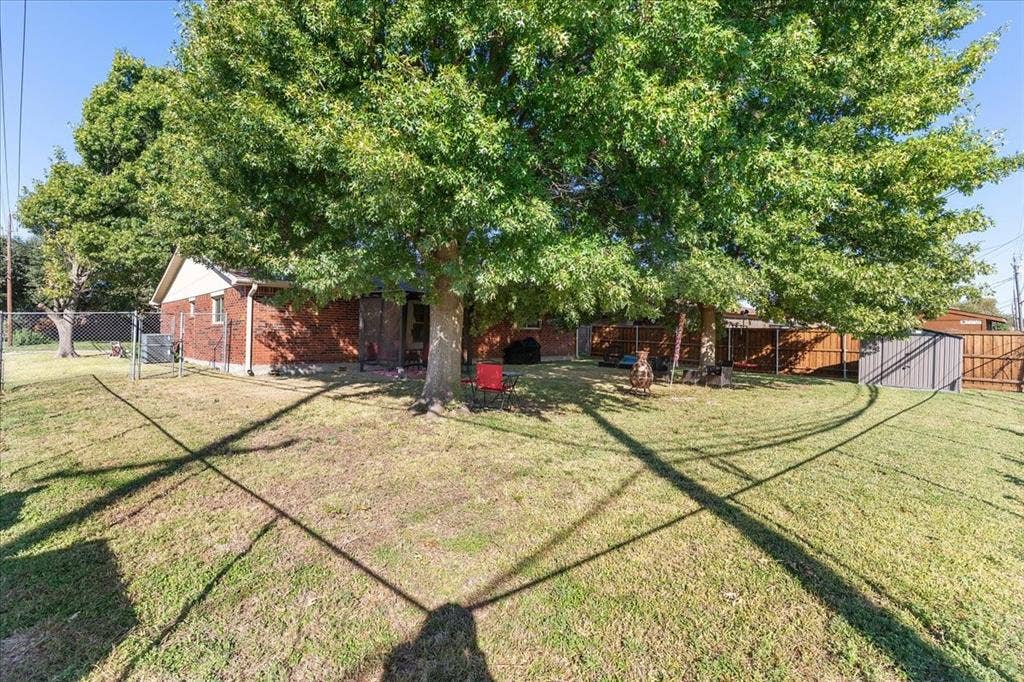 2702 Pebble Beach Drive, Lancaster, TX 75134 Fenced backyard featuring mature trees, brick exterior construction, and a metal storage shed