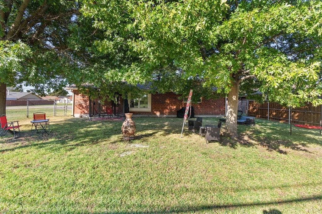 2702 Pebble Beach Drive, Lancaster, TX 75134 Rear exterior featuring red brick masonry, mature shade trees, a covered patio area, and perimeter wood fencing