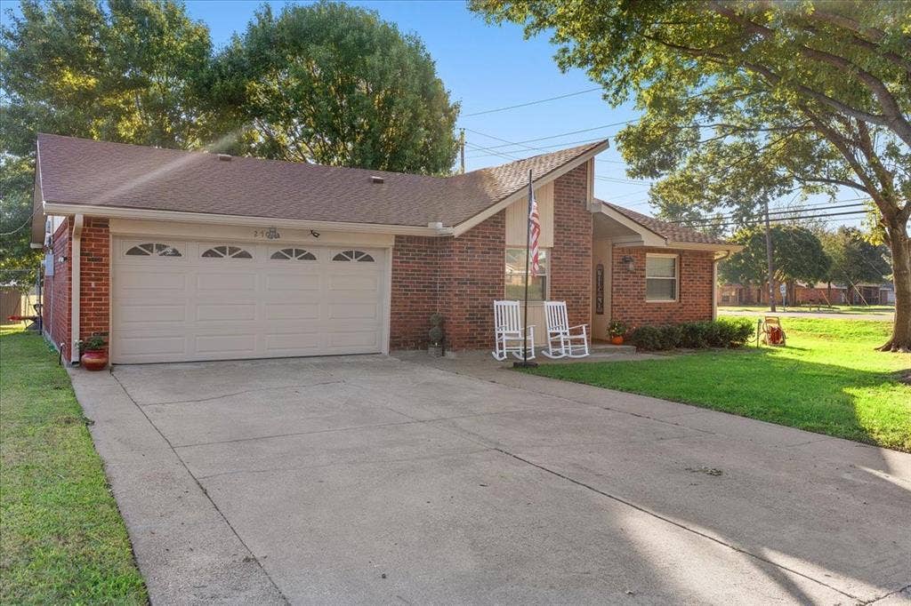 2702 Pebble Beach Drive, Lancaster, TX 75134 Single-story brick exterior featuring an attached two-car garage with arched panel detailing, a steep-pitched roofline, and a concrete driveway
