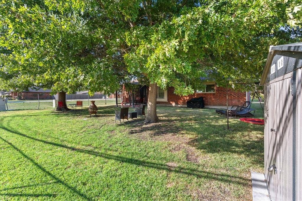 2702 Pebble Beach Drive, Lancaster, TX 75134 Expansive backyard featuring a lawn, mature trees, brick exterior cladding, and an outdoor storage structure