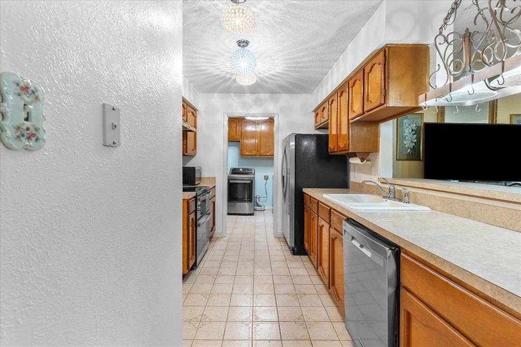 2702 Pebble Beach Drive, Lancaster, TX 75134 Kitchen featuring wood cabinetry, tile flooring, stone-surfaced countertops with an integrated double sink, and decorative globe lighting fixtures