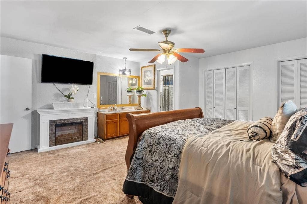 2702 Pebble Beach Drive, Lancaster, TX 75134 Electric fireplace with a white mantel, vanity with wood cabinetry and framed mirror, louvered closet doors, and ceiling fan with integrated lighting