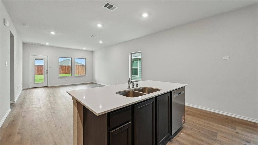 2620 Ocean View Grove, Crandall, TX 75114 Kitchen island featuring a double-basin stainless steel sink, integrated dishwasher, and light-toned solid surface countertop