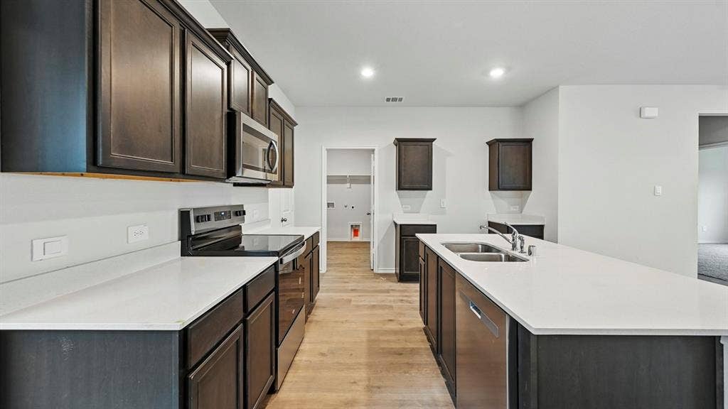2620 Ocean View Grove, Crandall, TX 75114 Open-concept kitchen featuring an expansive island with a double basin sink, dark wood-finish cabinetry, stainless steel appliances, light countertops, and wood-finish flooring