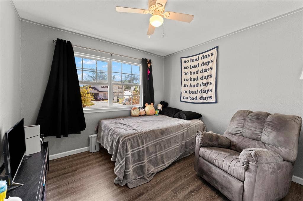 Room featuring neutral-toned walls, wood-finish flooring, a double-hung window, and a ceiling-mounted fan with integrated lighting