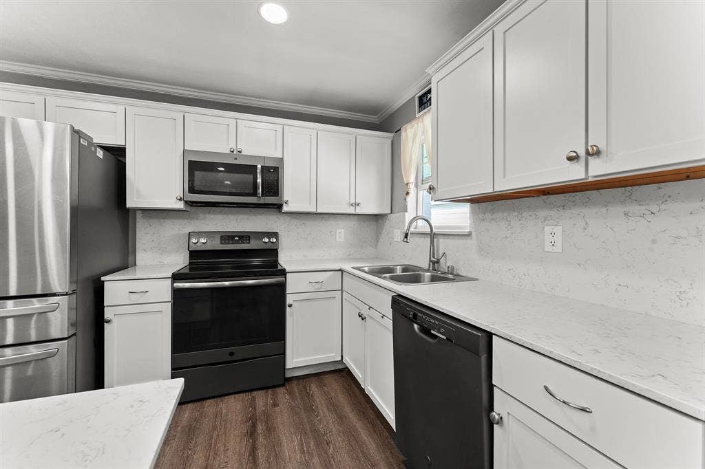 Kitchen featuring white cabinetry, quartz countertops with a subtle vein pattern, stainless steel appliances, a double-basin undermount sink, and wood-finish flooring